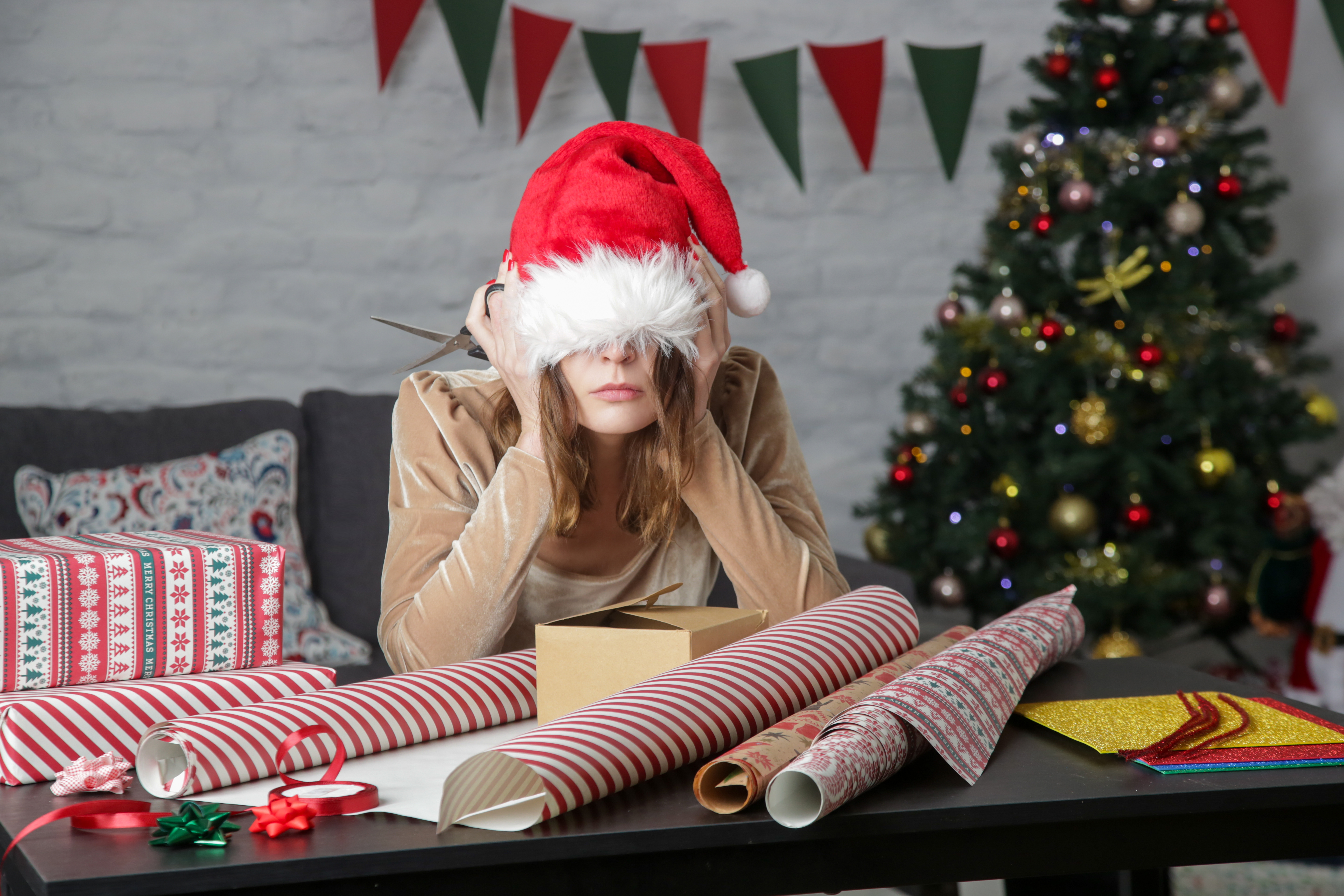 Gift wrapping supplies surrounding stressed woman in Santa hat