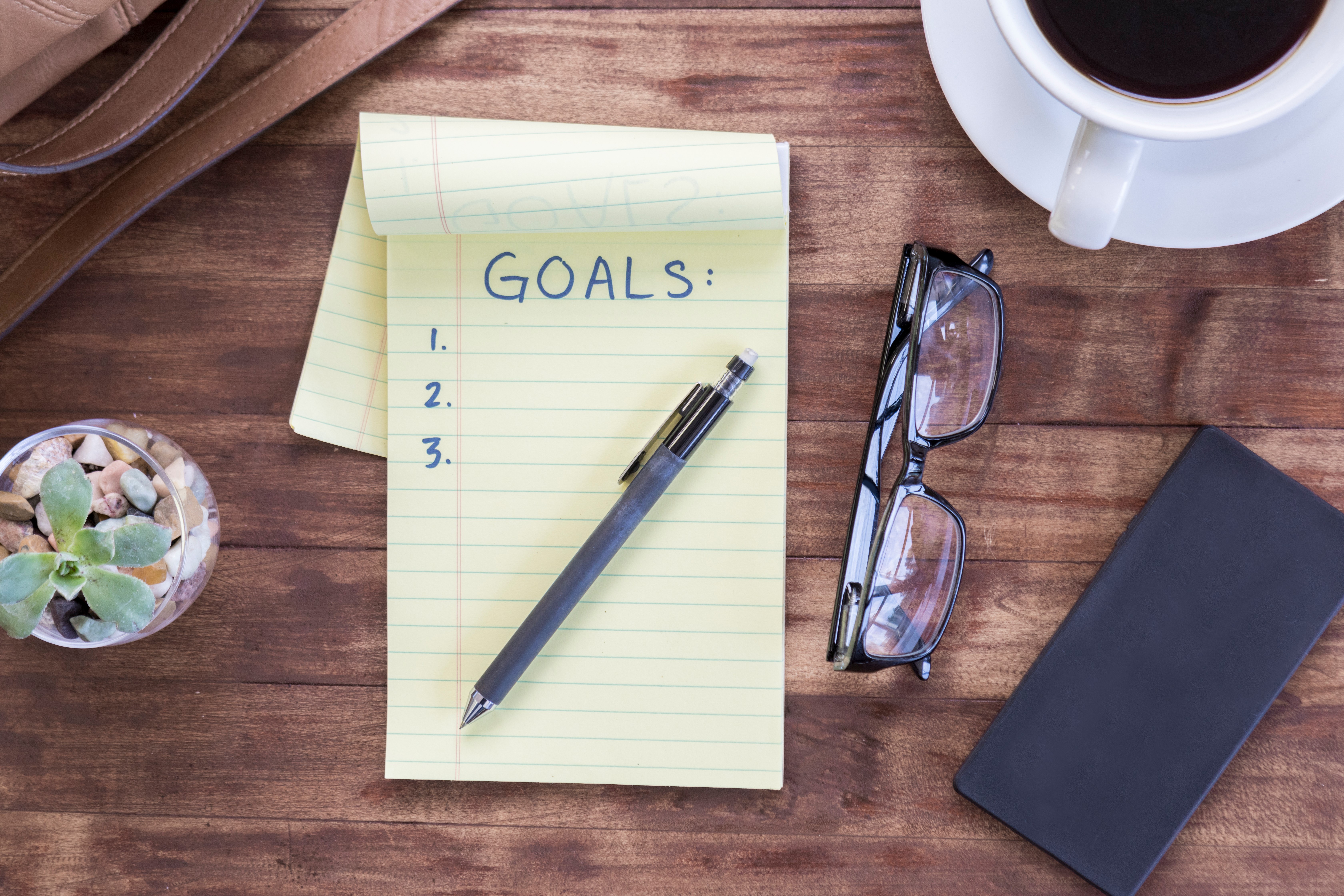 notepad that says goals and a pen on a desk